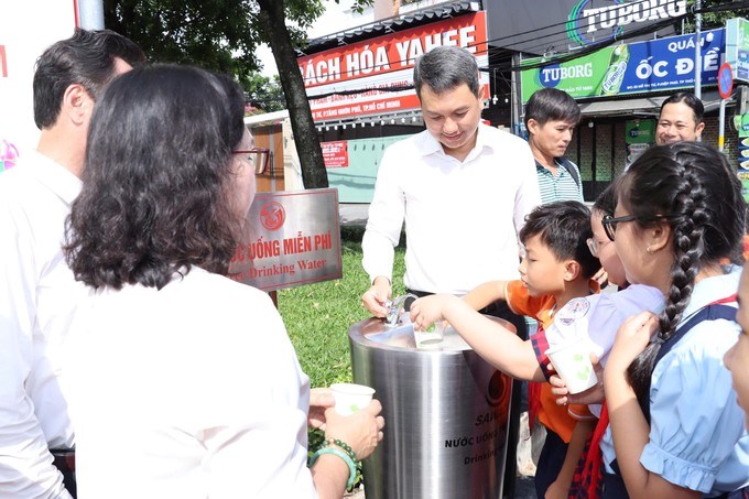 Lãnh đạo phường Tăng Nhơn Phú và các em học sinh trải nghiệm uống nước tại trụ nước uống miễn phí. Ảnh: THU HƯỜNG.