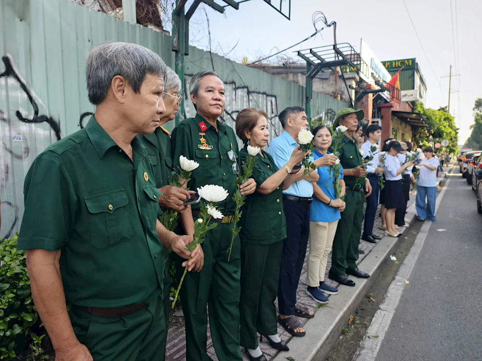 Người dân chờ tiễn đoàn xe đưa hài cốt liệt sĩ trên đường Cách Mạng Tháng Tám, khu vực giao lộ Điện Biên Phủ. Ảnh: NGUYỄN TÂN