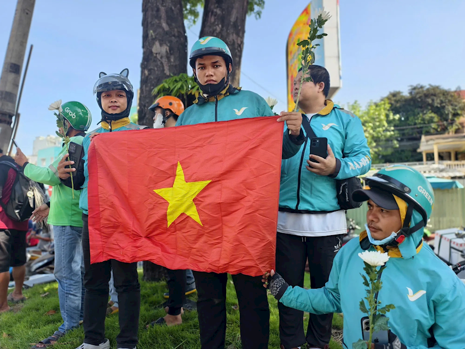 Các tài xế xe công nghệ chờ tiễn đoàn xe đưa hài cốt liệt sĩ tại vòng xoay Dân Chủ. Ảnh: NGUYỄN TÂN